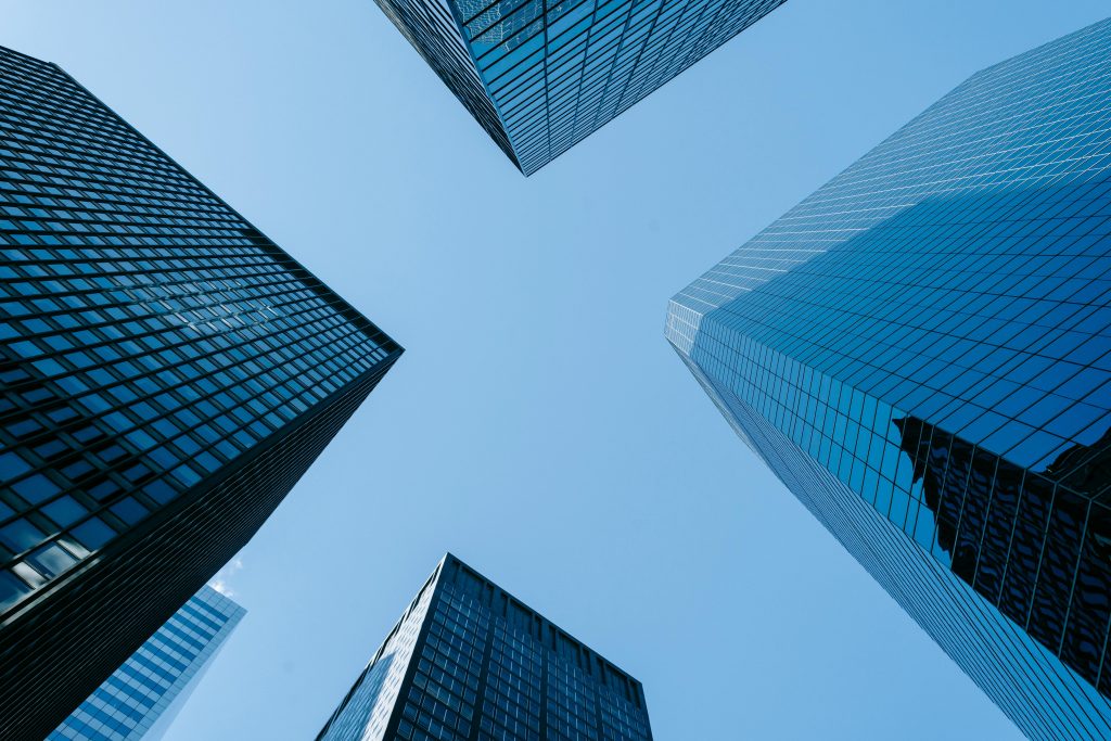 Low angle of high business towers with glass mirrored windows located in megalopolis downtown against blue sky